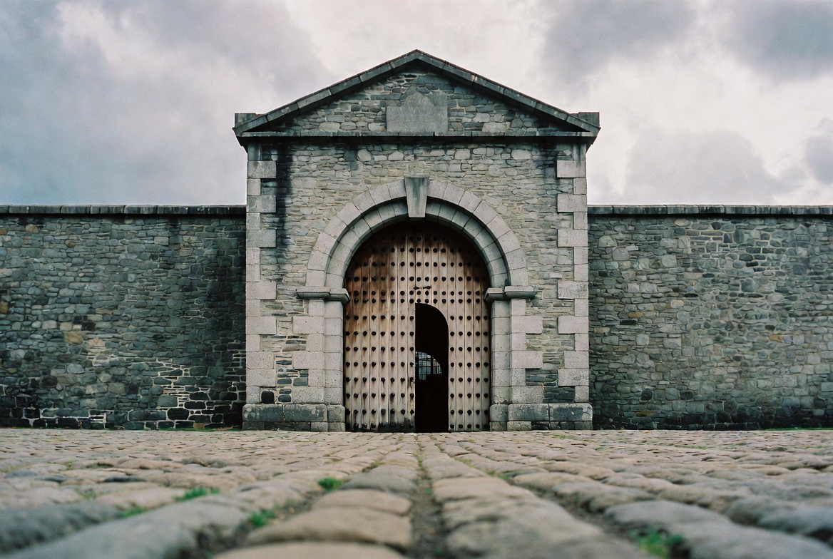 The grey limestone facade and barred windows of Kilmainham Gaol photographed from across the cobbled forecourt at first light.