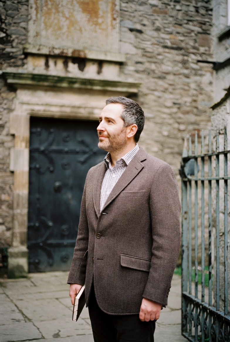 Dr Cormac Brennan, historian, standing in front of the limestone wall of an old courtyard.